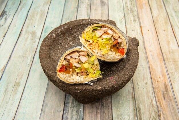 Huge Mexican burrito of fried chicken breast with rice and pico de gallo on volcanic stone molcajete