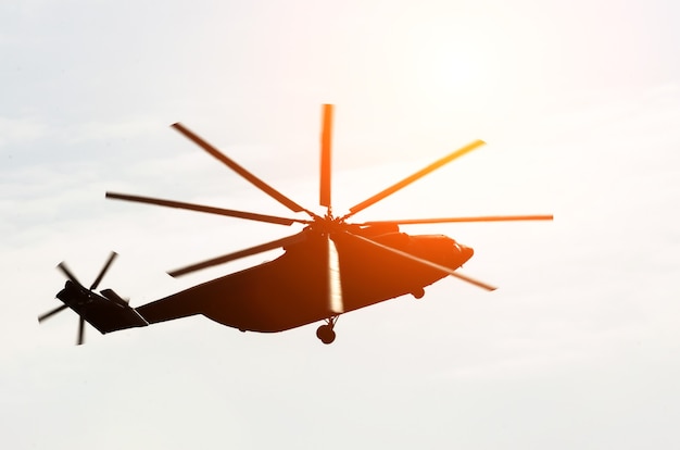 헬리콥터의 거대한 실루엣이 태양의 눈부신 하늘로 날아갑니다.