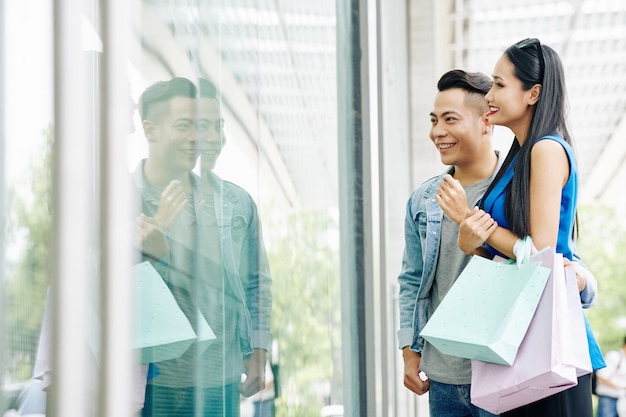 Hugging young beautiful couple with shopping bags looking at mannequins in shop window