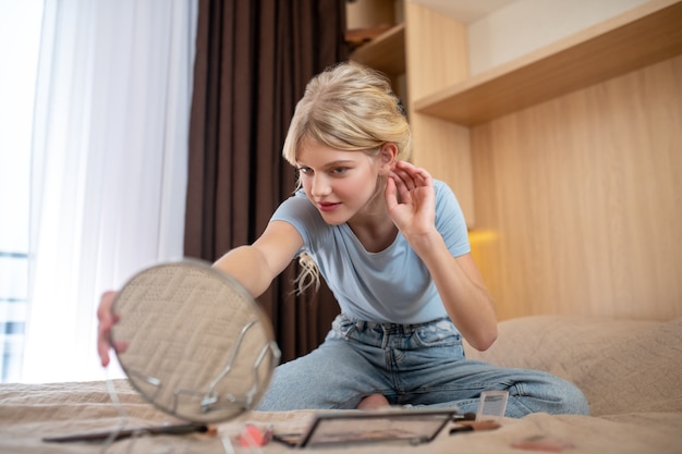 Huid problemen. Een meisje in een blauw shirt dat op haar bed zit en in de spiegel kijkt en pooiers vindt