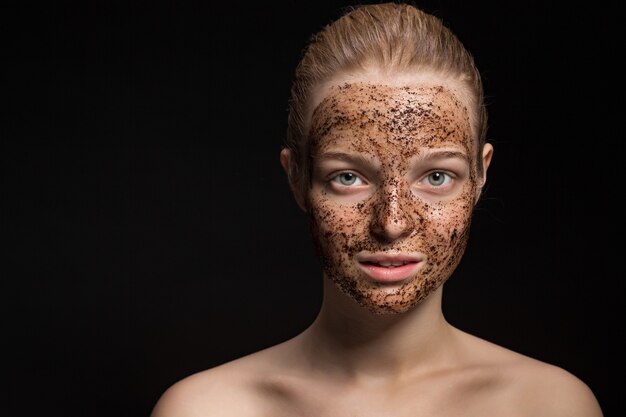 Foto huid scrub koffiedik masker op het gezicht van een mooie jonge vrouw