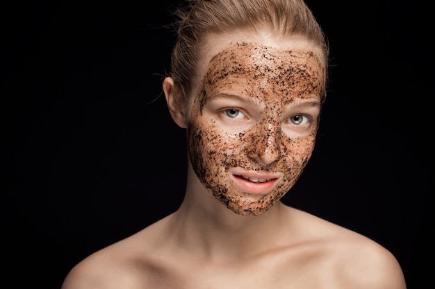 Huid scrub koffiedik masker op het gezicht van een mooie jonge vrouw