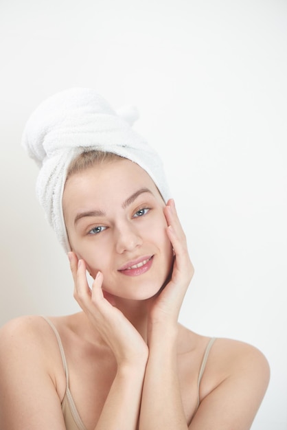 Huidsverzorging. Jonge vrouw op witte achtergrond met handdoek op hoofd wat betreft haar schone huid op het gezicht