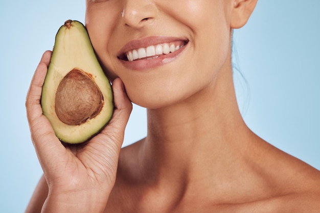 Huidverzorging schoonheid en glimlach vrouw met avocado natuurlijke make-up en gezichtsdetox op blauwe achtergrond Gezondheid wellness en mond van model organische luxereiniging en cosmetica met fruit in studio