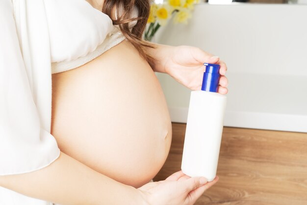 Huidverzorging tijdens de zwangerschap. Dispenser met crème in de hand voor striae op het lichaam. Hoge kwaliteit foto