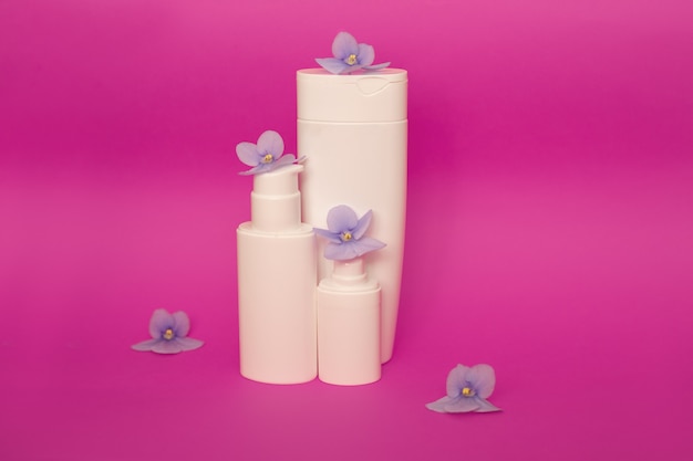 Huidverzorging verpakking mockup op een roze achtergrond tussen violette bloemen. Plat leggen. Cosmetische schoonheid natuurlijk. Gezichts- en lichaamsbehandeling. Kopieer ruimte. Vooraanzicht.