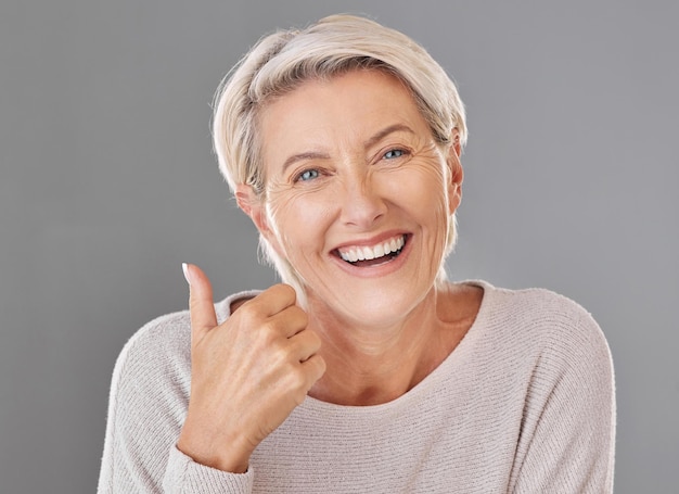 Huidverzorging wellness en duimen omhoog door gelukkige volwassen vrouw die lacht met winnend handgebaar tegen studio achtergrond Senior ondersteuning en aanbevelen cosmetische chirurgie behandeling of product voor rimpels