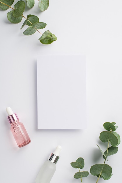 Huidverzorgingsconcept Bovenaanzicht verticale foto van papieren kaart roze en witte transparante glazen druppelflessen en eucalyptus op geïsoleerde witte achtergrond met copyspace
