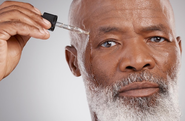 Huidverzorgingsportret en man met gezichtsolie in een studio voor een natuurlijke schoonheid en huidbehandeling Cosmetische gezondheid en senior man model met gezichtsserum voor een wellnessroutine tegen een grijze achtergrond