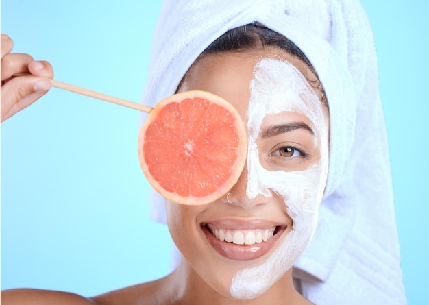 Huidverzorgingsportret en vrouw met grapefruitmasker in studio voor schoonheidshaar en cosmetica op blauwe achtergrond Gezichtsgezicht en meisjesmodel ontspannen in fruitluxe en productwellness of geïsoleerd