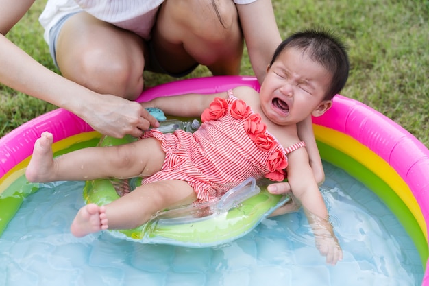 Huilende baby gedragen door moeder die geniet in het opblaasbare zwembad