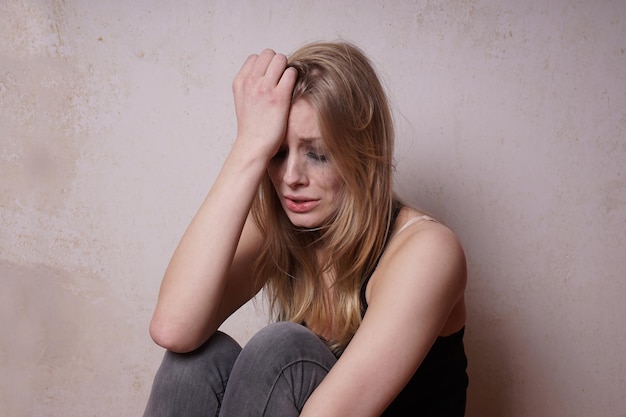 Huilende jonge vrouw zit tegen de muur.