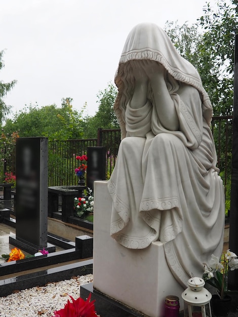 Huilende vrouw Sculptuur op de begraafplaats De figuur van een moeder vrouw of vrouw in een kap of stal Klaagzang om de overledene Grafsteen op een christelijk graf Verdriet en verdriet