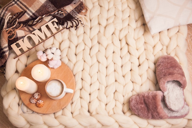 Huis bont pantoffels. kopje cappuccino en koekjes, kaarsen, geruite plaid, inscriptie Home op de deken van dik garen met kopieerruimte. De sfeer van huiselijkheid en comfort