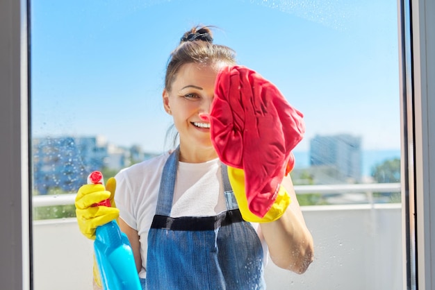 Huis die rijpe vrouw in rubberhandschoenen schoonmaken die een schort dragen die vensters wassen