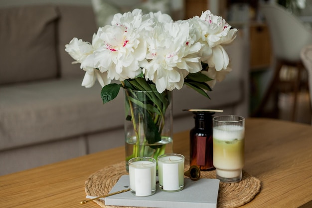 Huis gezellig interieur Kaarsen een boeket pioenrozen in een glazen vaas een glas matchalate op een houten salontafel Lente