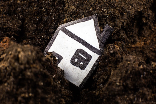 Huis in de grond, vallend in een scheur in de aarde. oncept van aardbeving en verlies van een huis. schulden herstellen.