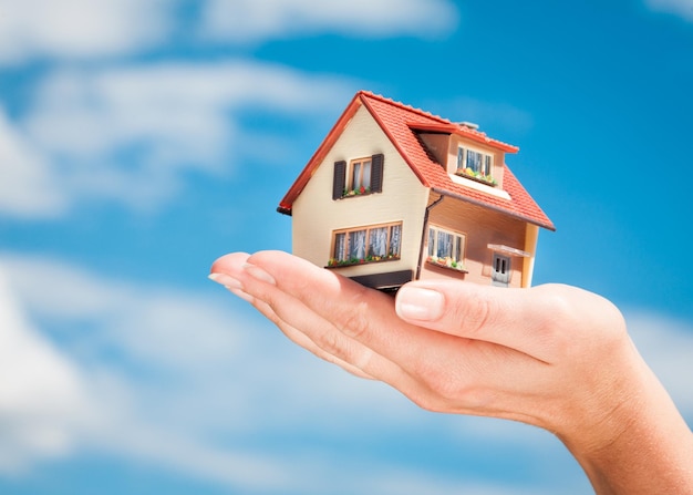 Huis in de handen van de man op een achtergrond van blauwe lucht