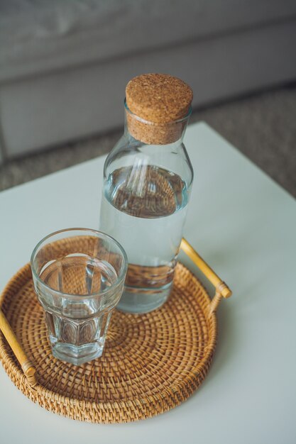 Huis interieur. Een glazen fles met water, een glas, een rotan rieten dienblad op een salontafel. Knus.