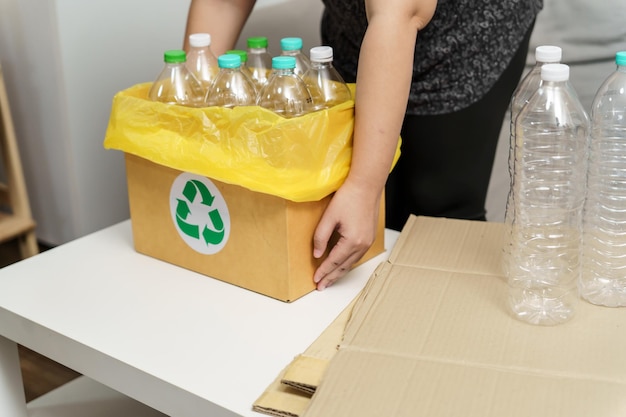 Huis recycle eco groene nul concept Vrouw gooit lege plastic fles in recyclingbak met gele vuilniszakken thuis