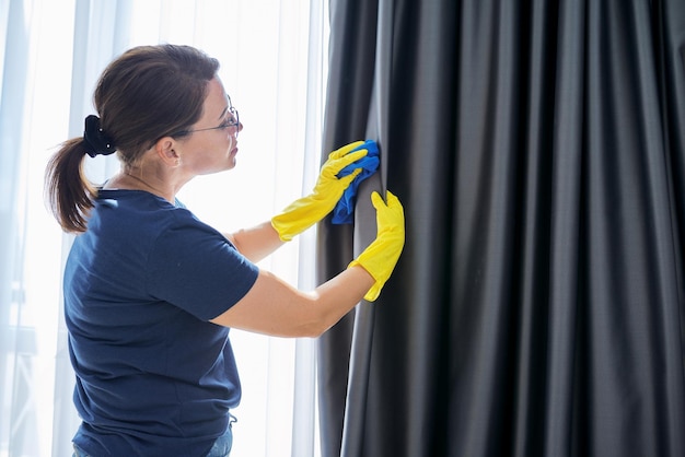 Huis schoonmaken, vrouw in handschoenen met een vod die gordijnen schoonmaakt. Huishoudelijk werk, huishouden, huishouden, netheidsconcept