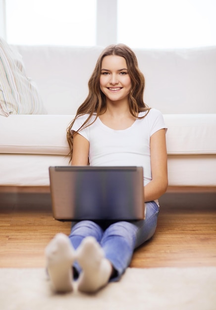 huis, technologie en internet concept - glimlachend tienermeisje zittend op de vloer met laptopcomputer thuis