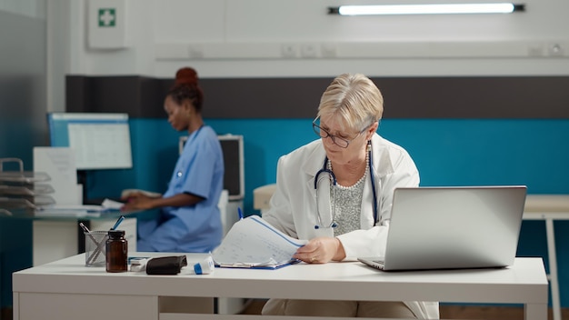 Huisarts die werkt met afspraakrapport op laptop, diagnose-informatie gebruikt om receptgeneesmiddelen voor herstel te plannen. Medische expertise en gezondheidszorgsysteem om ziekten te genezen.