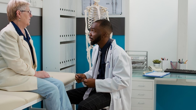 Huisarts kijkt naar bottenröntgenfoto's met senior patiënt, analyseert de diagnose van radiografiescans om gezondheidszorgbehandeling en ondersteuning te geven. Mannelijke arts en oude vrouw praten over ziekte.