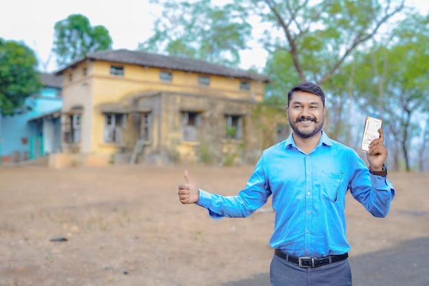 Huisconcept kopen Indiase man met een Indiaas briefje in de ene hand en staat voor het huis