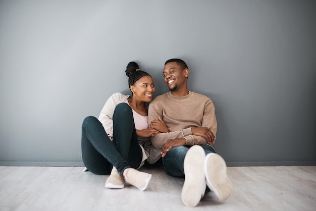 Huiseigenaar liefde en beginnend met een zwart stel dat samen zit in hun nieuwe huis op een grijze muur achtergrond Onroerend goed kamer en hypotheek met een man en vrouw op de vloer na verhuizing