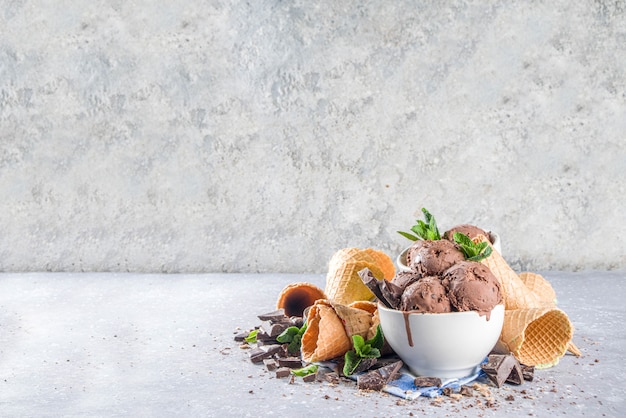 Huisgemaakt chocoladeroomijs met stukjes chocolade en schaafsel, en ijshoorntjes. In kleine witte kommen op witgrijze stenen tafel kopieerruimte