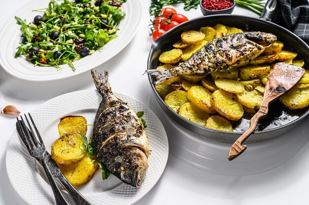 Huisgemaakt diner met gebakken Dorado vis, rucola salade met tomaten, gebakken aardappelen. bovenaanzicht