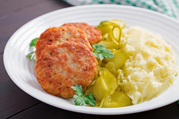 Huisgemaakte gebakken cutlets vleesballen met aardappelpuree en ingelegde komkommer op een wit bord