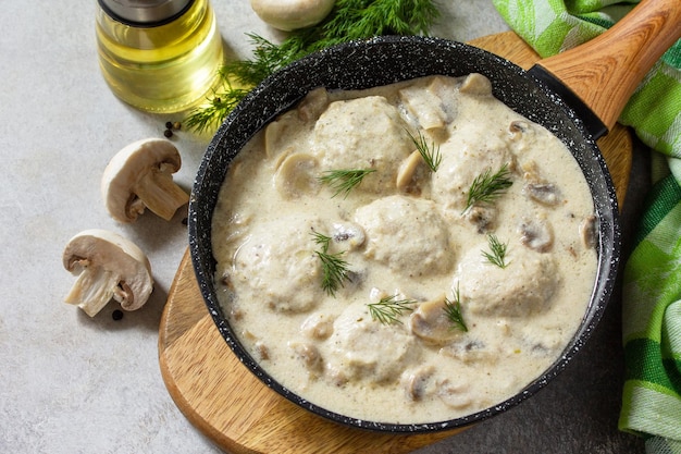 Huisgemaakte gehaktballen in zure roomsaus met champignons in een pan op stenen of leistenen tafel