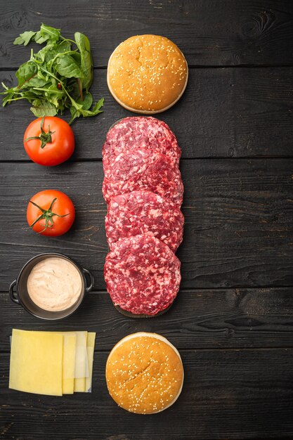 Huisgemaakte hamburger. Rauwe runderpasteitjes, sesambroodjes met andere ingrediënten, op zwarte houten tafel