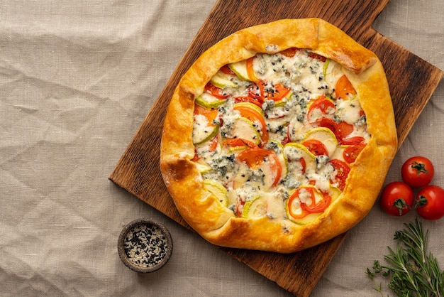 Huisgemaakte hartige galette met groenten, tarwetaart met tomaten, courgette, blauwe kaas gorgonzola. rustieke korstcrostata op donker linnen textieltafelkleed.