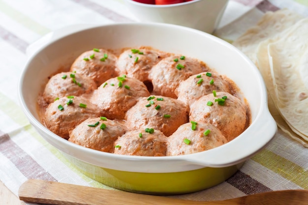 Huisgemaakte kipgehaktballetjes gebakken in romige tomatensaus in keramische ovenschaal