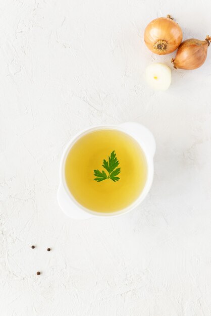 Huisgemaakte kippenbouillon in een wit bord op een witte tafel