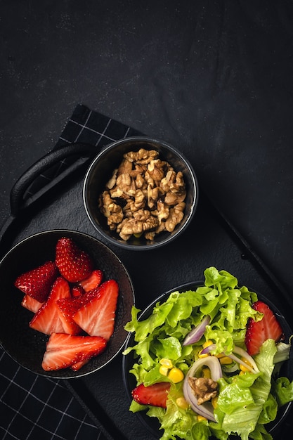 Huisgemaakte Salade met sla, aardbeien, rode ui, maïs; olijfolie en walnoten in een kom. Veganistisch eten concept