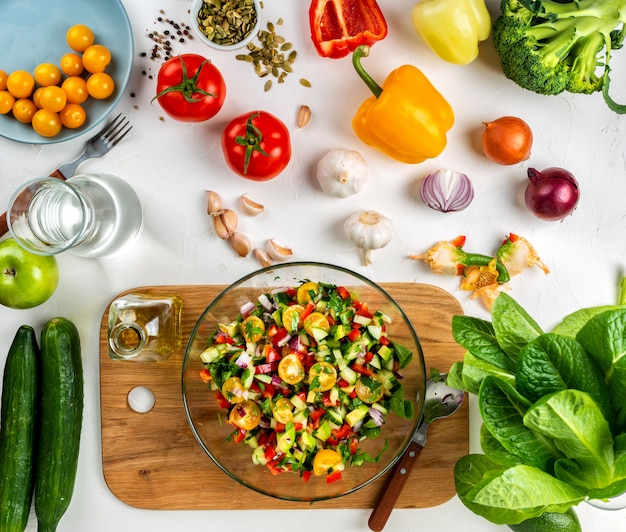 Huisgemaakte salade van verschillende biologische groenten in een glazen kom met ingrediënten en kruiden
