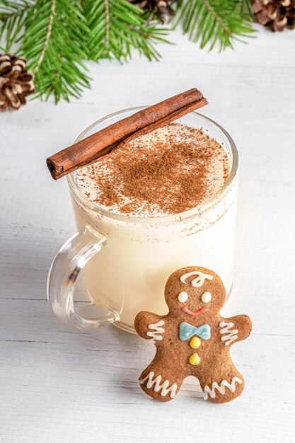 Foto huisgemaakte xmas eggnog met kaneel in glazen beker met gember man op witte houten achtergrond