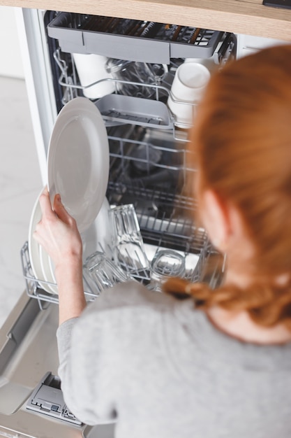 Huishoudelijk werk: jonge vrouw die gerechten in de vaatwasser zet