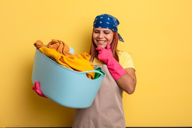 Huishoudster glimlachend met een gelukkige zelfverzekerde uitdrukking met de hand op de kin die kleding wast concept