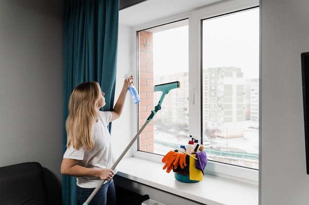 Huishoudster sproeit thuis wasmiddel en maakt ramen schoon Huisvrouw vrouw maakt thuis schoon en wast ramen Huisschoonmaakservice