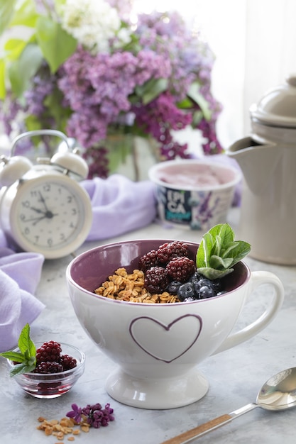 Huismuesli met bessen op de tafel bij het raam met een boeket seringen.