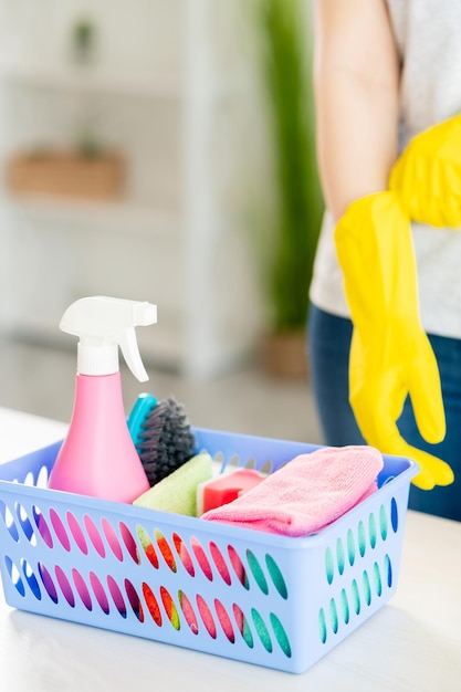 Huisreiniging Wasmiddelhulpmiddelen Huishoudelijke klusjes Onherkenbare vrouw in beschermende handschoenen in de buurt van mand met schonere spray zeepachtige sponzen borstel microvezeldoek op tafel