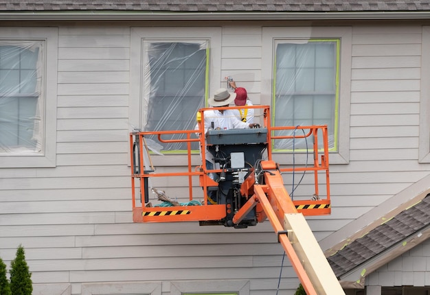 Huisschilders die verfspuiten van de hoogwerker gebruiken