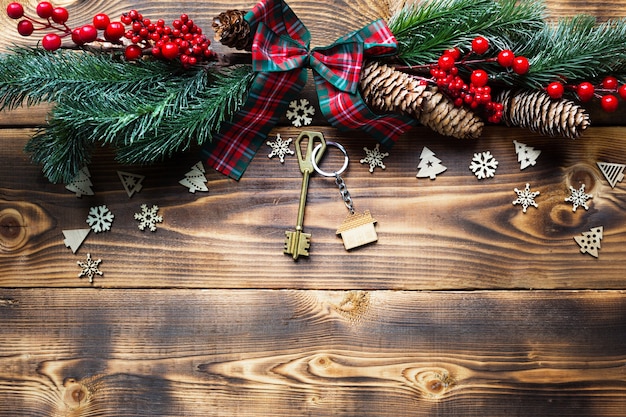 Huissleutel met sleutelhanger huisje op een feestelijke milieuvriendelijke, natuurlijke achtergrond met kerstboom. Gelukkig Nieuwjaar-rode achtergrond, cadeau, wenskaart. Aankoop, bouw, verhuizing, hypotheek