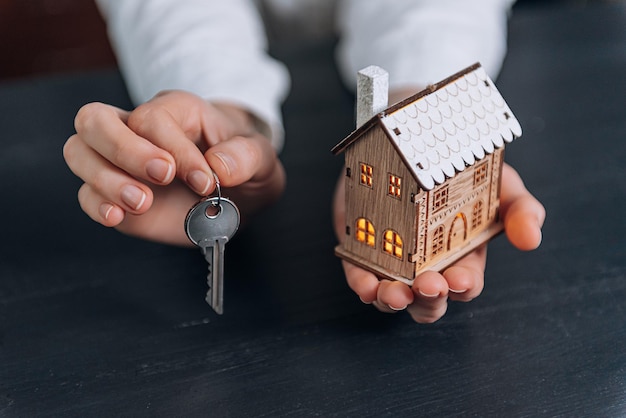 Huissleutels in de handen van een vrouw en een klein model van een huis met lichtgevende ramen in de buurt. concept van het verwerven van uw huis