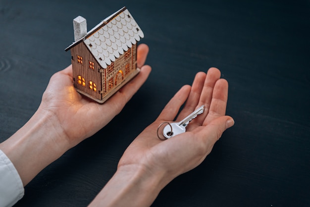 Huissleutels in handen van een vrouw en een klein model van een huis met lichtgevende ramen in de buurt. concept van het verwerven van uw huis